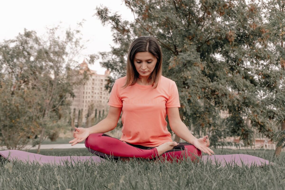 A woman meditatively practices yoga in a peaceful park setting, surrounded by trees and grass.
