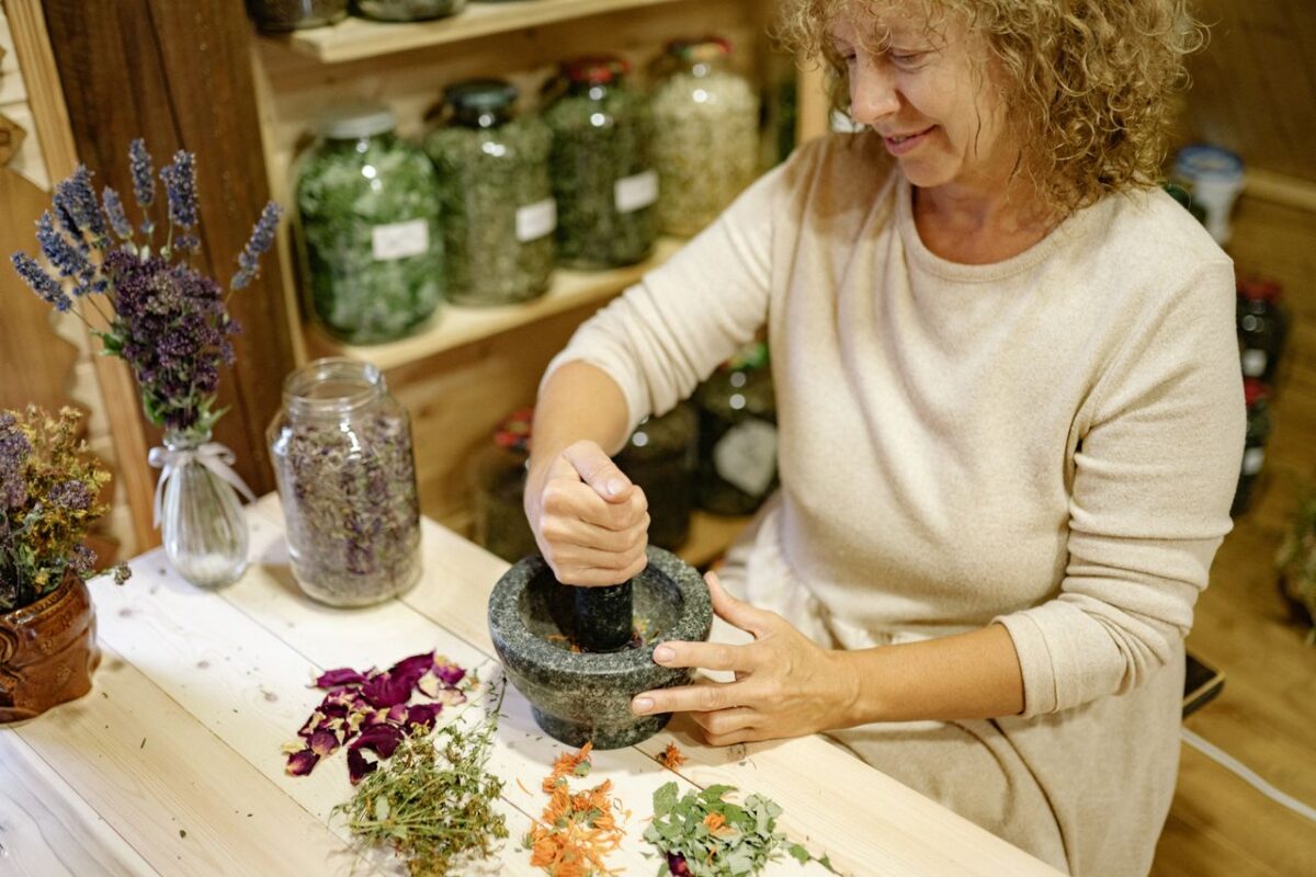 about-002 A woman using a mortar and pestle to prepare herbs in a rustic indoor setting.